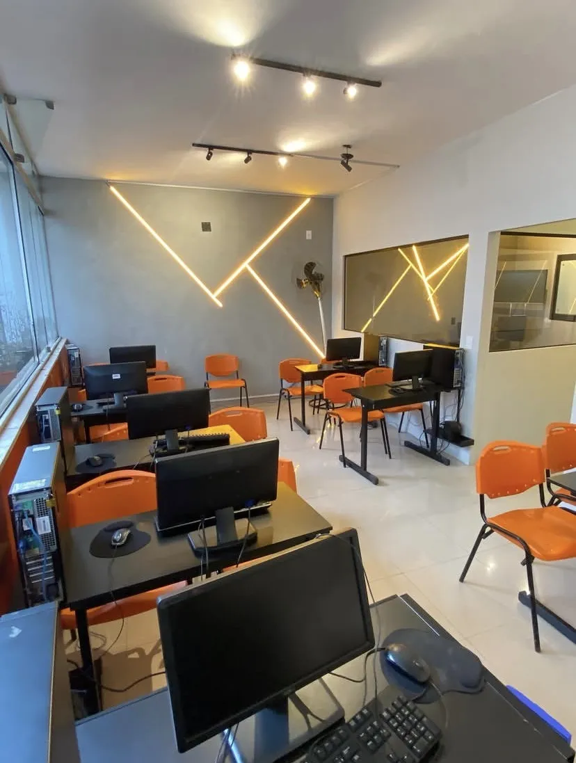Laboratório de informática da unidade com computadores e cadeiras laranja