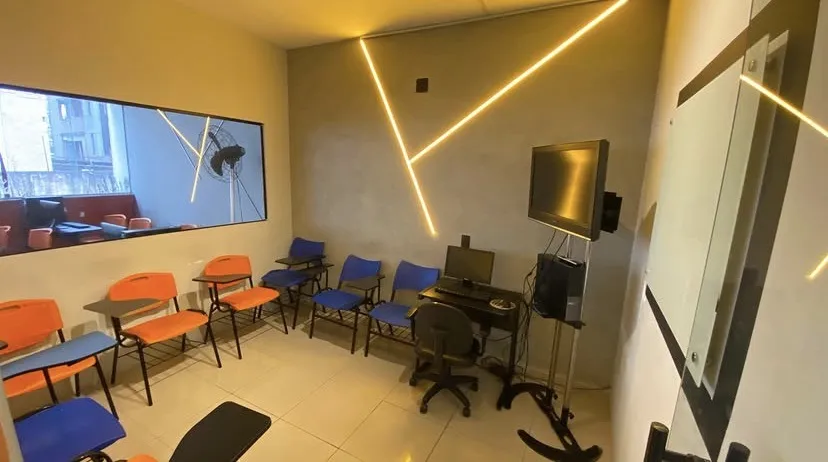 Sala com TV, lousa e cadeiras laranja e azuis