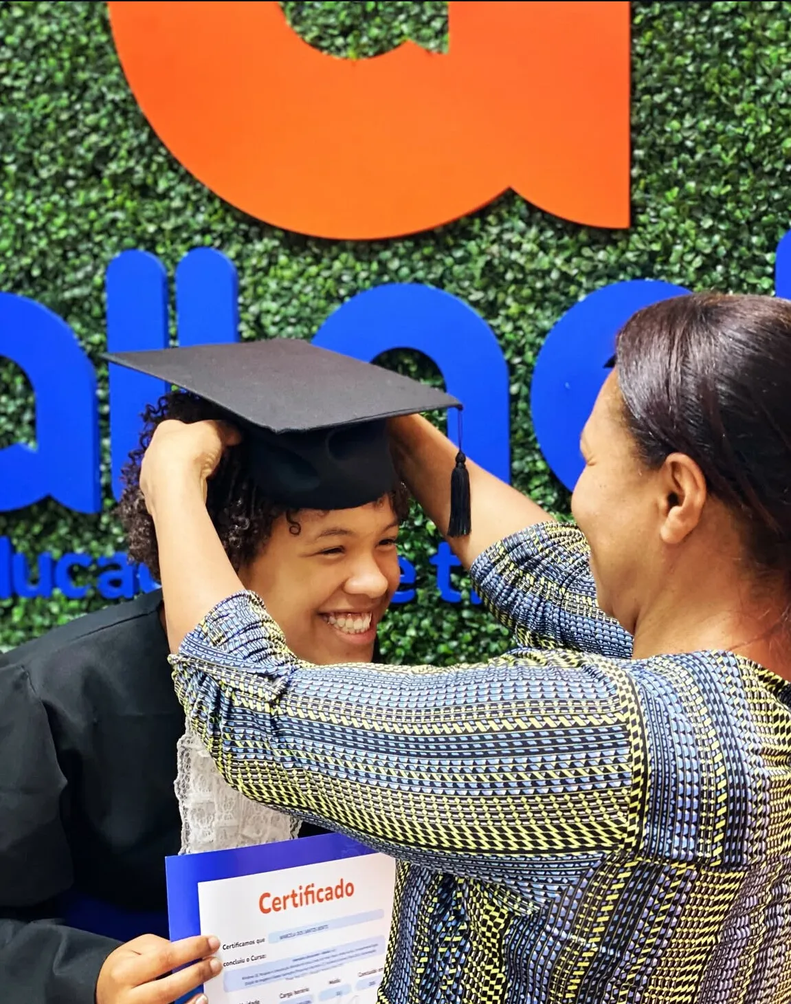Aluna recebendo o capelo na formatura da All Net, diante do painel com o logo